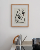 all-groups - Small oak-framed Swan print hanging on a white wall above a kitchen counter, with a steel jug with a wooden handle and a steel pot on the hob below.